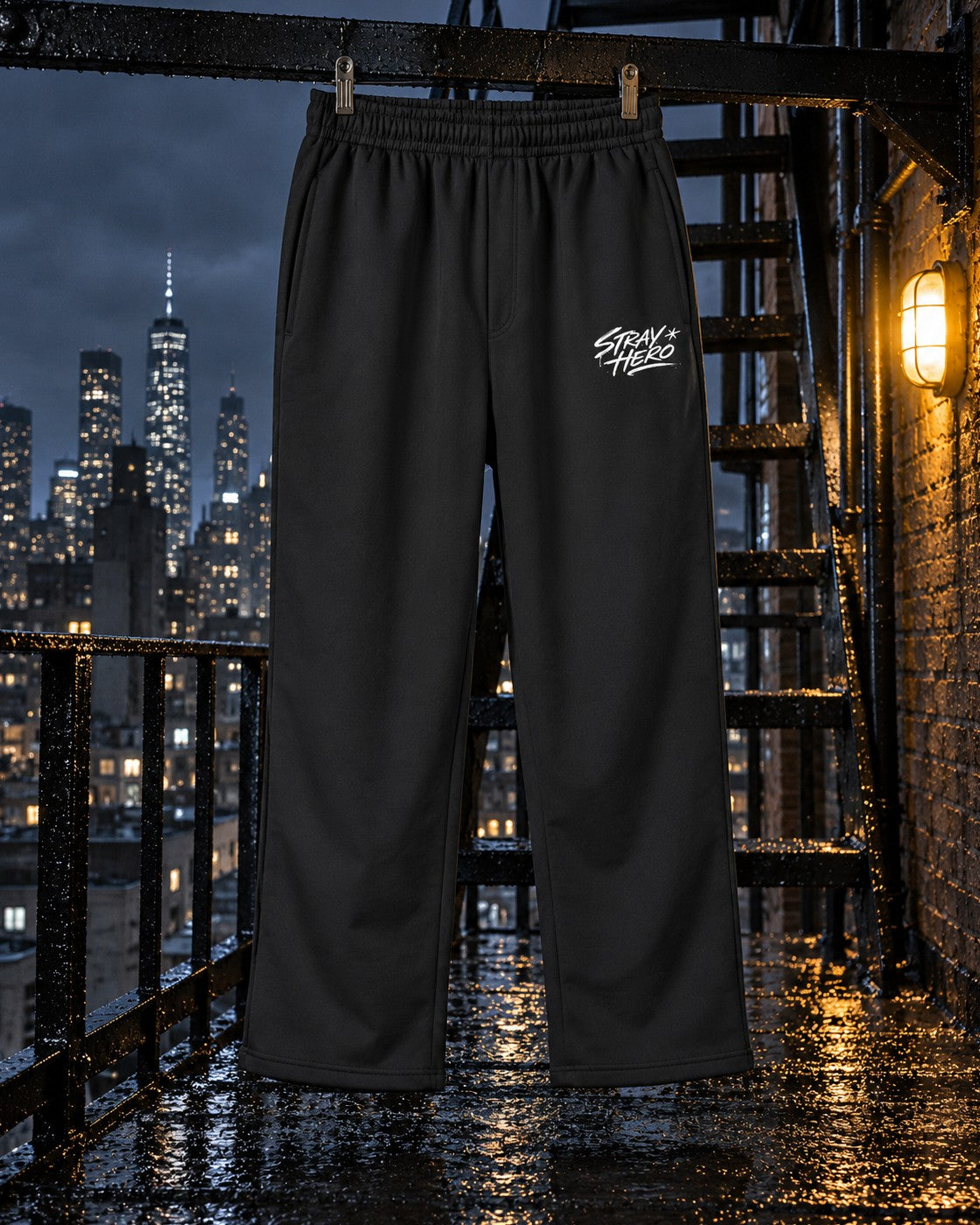 Script Track Joggers, leg print, black, hanging on a fire escape railing beside a wall lamp at night — AI-generated visual