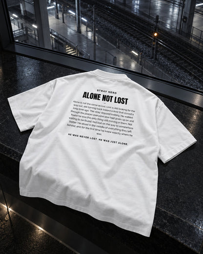 Alone Not Lost Story Tee White, back print, white, laid on a bench on a train platform at night — AI-generated visual