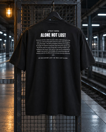 Alone Not Lost Story Tee Black, back print, black, hanging on a fence under a lamp on a train platform — AI-generated visual