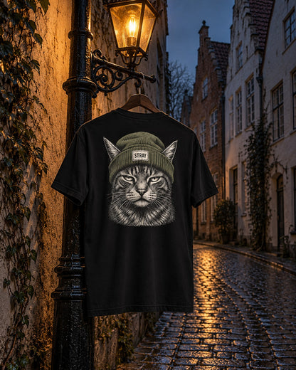 Beanie Cat Tee Shade, back print, black, hanging on a street lamp in an old-town lane with gabled houses at dusk — AI-generated visual