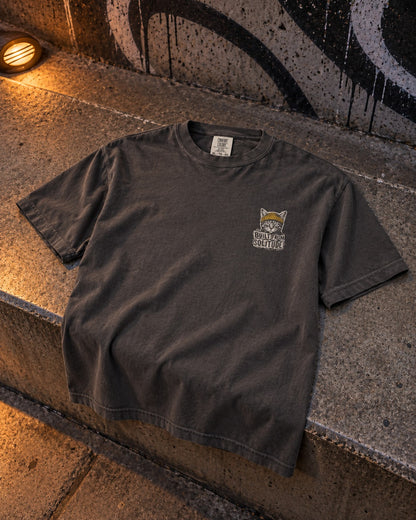 Built From Solitude Graffiti Tee, front print, graphite, laid on a concrete ledge at a skatepark under a wall lamp at night — AI-generated visual