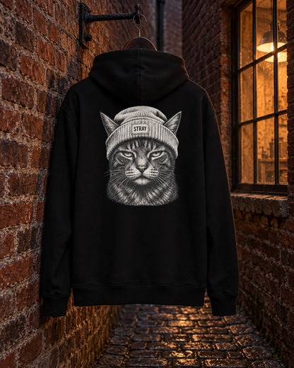 Beanie Cat Hoodie Ghost, back print, black, hanging on a brick wall beside a lit workshop window in a cobbled lane at night — AI-generated visual