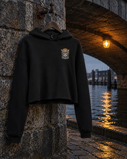 Cat Badge Ember Crop Hoodie, front print, black, hanging on a stone pier under a bridge arch by the water at night — AI-generated visual