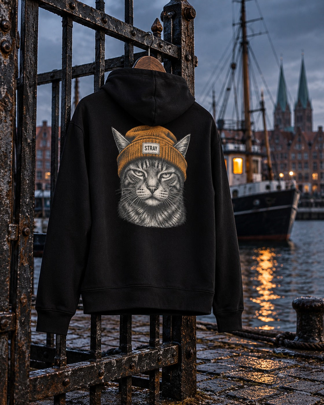 Beanie Cat Hoodie Ember, back print, black, hanging on an iron harbour gate with tall ships behind at dusk — AI-generated visual