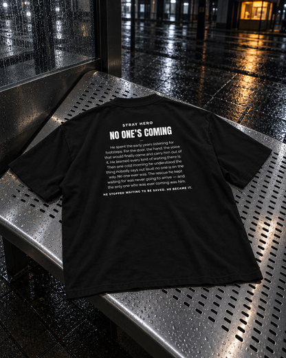 No One's Coming Story Tee Black, back print, black, laid on a metal bench at a bus stop — AI-generated visual
