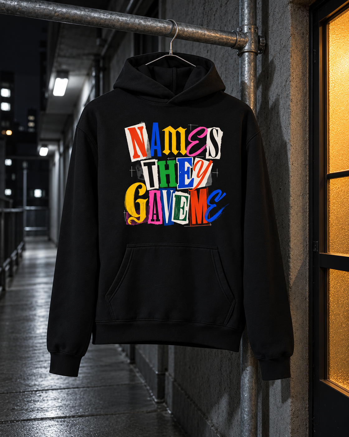Names They Gave Me Hoodie, front print, black, hanging on a rail in a hallway at night — AI-generated visual