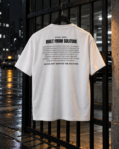 Built From Solitude Story Tee White, back print, white, hanging on a metal gate at night — AI-generated visual