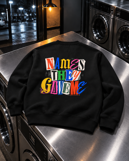 Names They Gave Me Sweatshirt, back print, black, laid on a steel counter in a laundromat — AI-generated visual