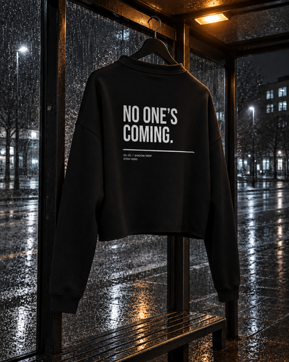 No One's Coming Crop Hoodie, back print, black, hanging at a bus shelter in the rain — AI-generated visual