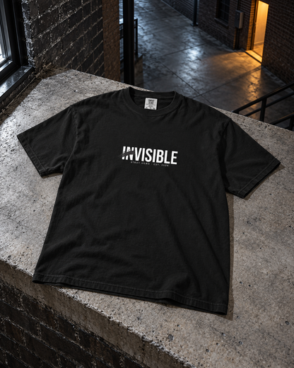 Invisible Tee, front print, black, laid on a stone ledge in a courtyard at night — AI-generated visual