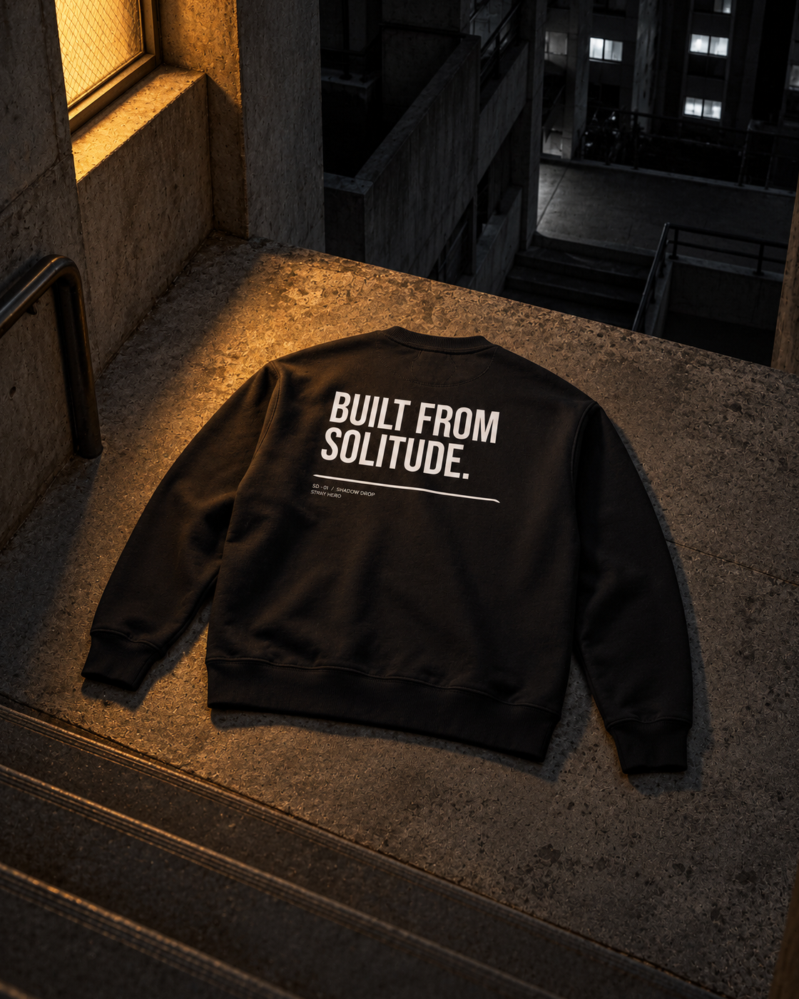 Built From Solitude Sweatshirt, back print, black, laid on concrete steps under a lamp at night — AI-generated visual