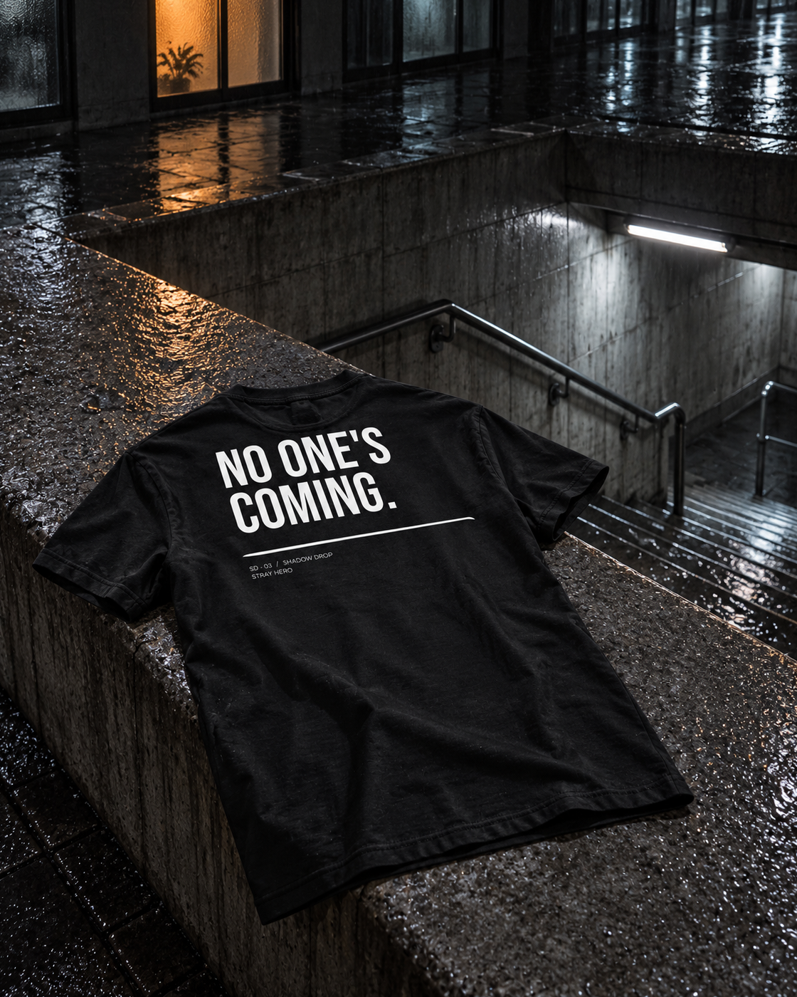 No One's Coming Tee Typography, back print, black, laid on a concrete ledge by an underpass — AI-generated visual