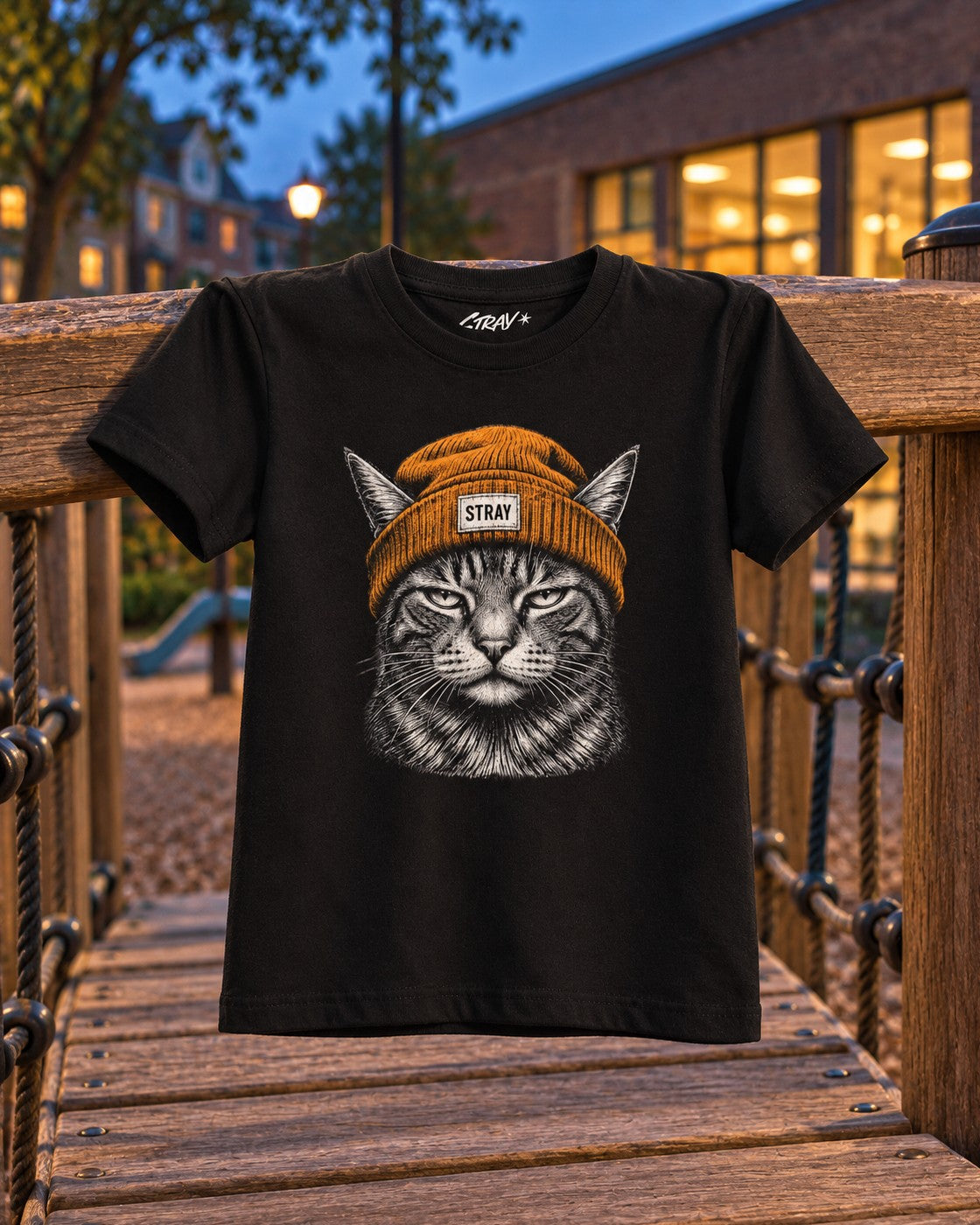 Ember Kids Tee, front print, black, hanging on a wooden playground bridge at dusk — AI-generated visual
