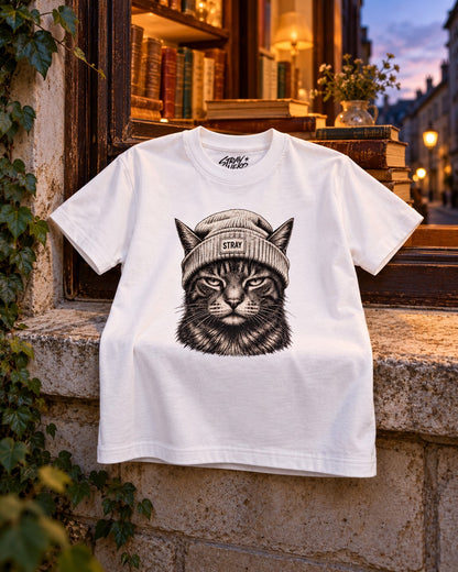 Ghost Kids Tee White, front print, white, draped on a stone window ledge below a lit bookshop window at dusk — AI-generated visual