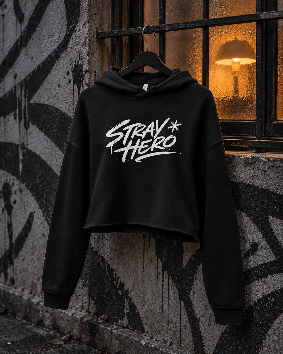 Tagger Crop Hoodie, front print, black, hanging on window bars on a graffiti wall at night — AI-generated visual