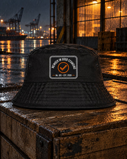 Loners Union Bucket Hat, front patch, black, on a wooden crate in front of a lit warehouse window at the harbour at night — AI-generated visual