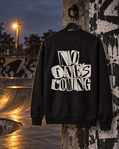 No One's Coming Sweatshirt Paste-Up, back print, black, hanging on a concrete pillar beside a skatepark at dusk — AI-generated visual