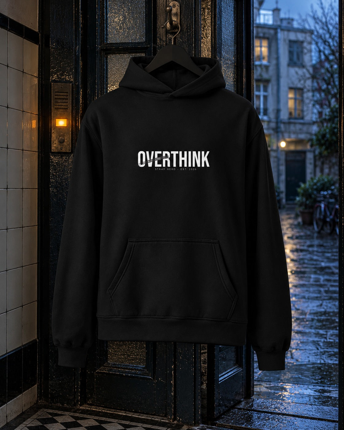 Overthink Hoodie, front print, black, hanging in the open doorway of a tiled stairwell at night — AI-generated visual