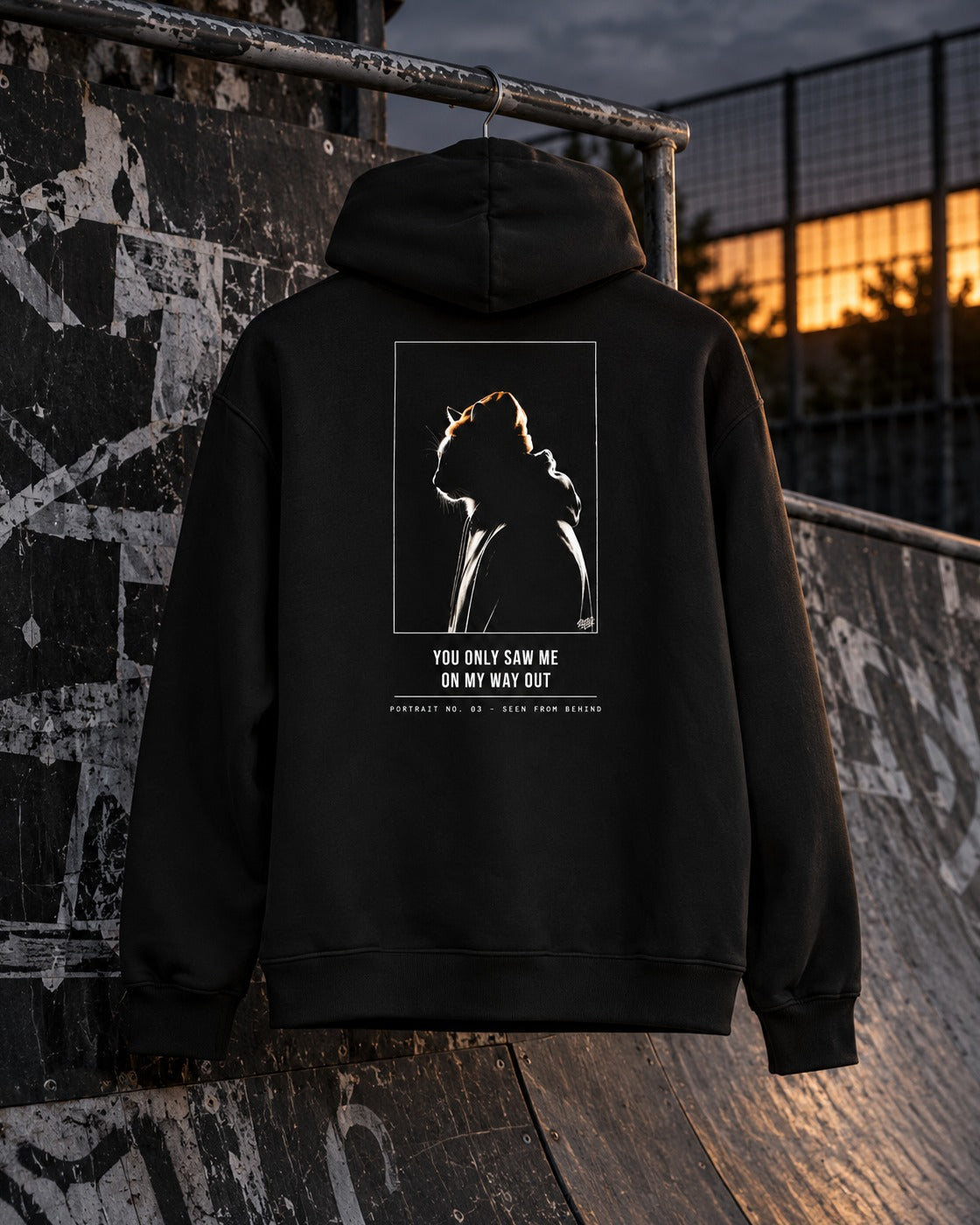 Portrait No. 03 Hoodie, back print, black, hanging on a rail at a skatepark ramp at dusk — AI-generated visual