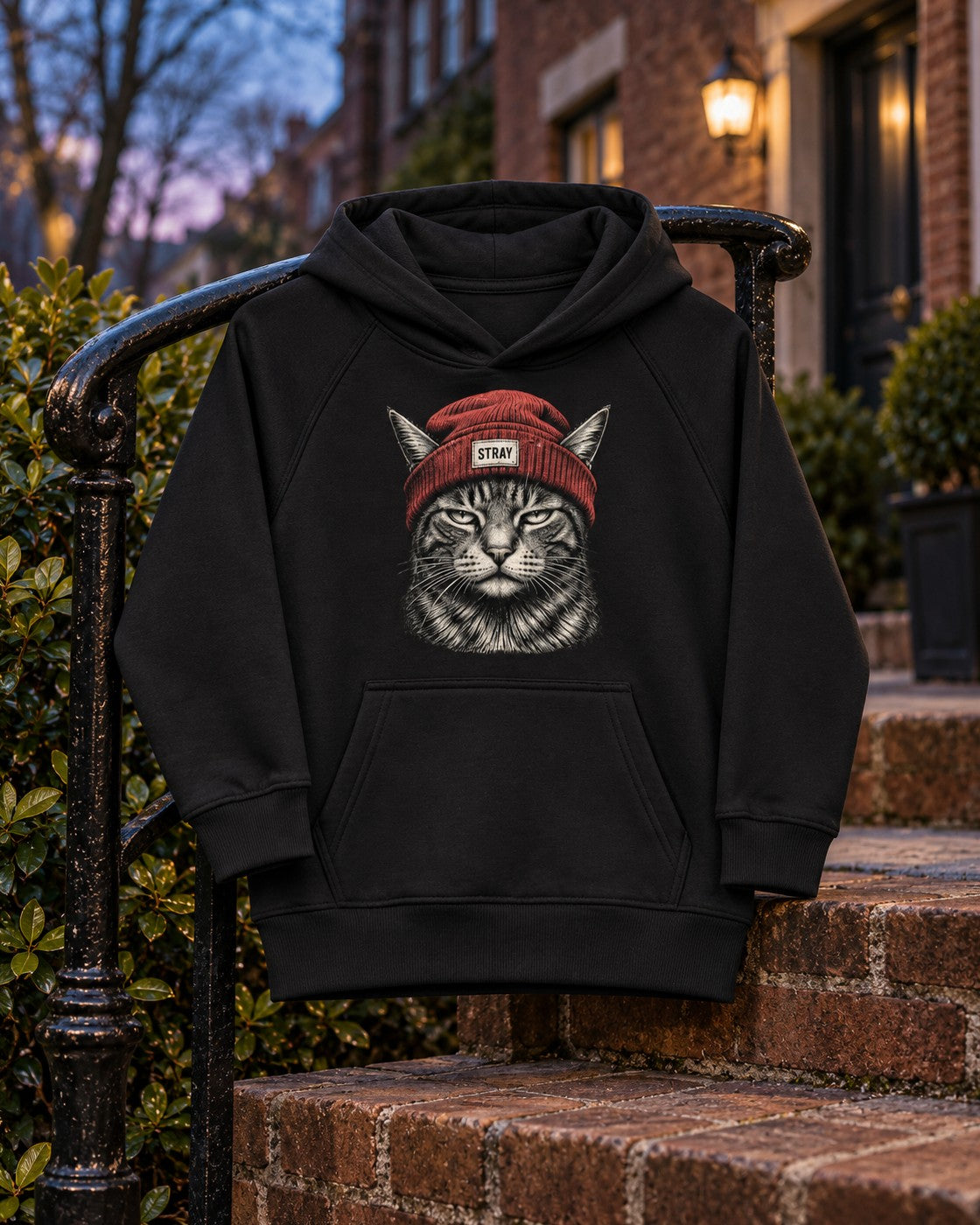 Rogue Kids Hoodie, front print, black, draped over an iron stair railing by brick steps at dusk — AI-generated visual