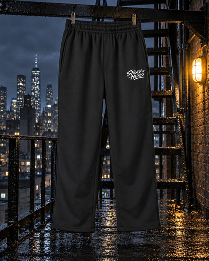 Script Track Joggers, leg print, black, hanging on a fire escape railing beside a wall lamp at night — AI-generated visual