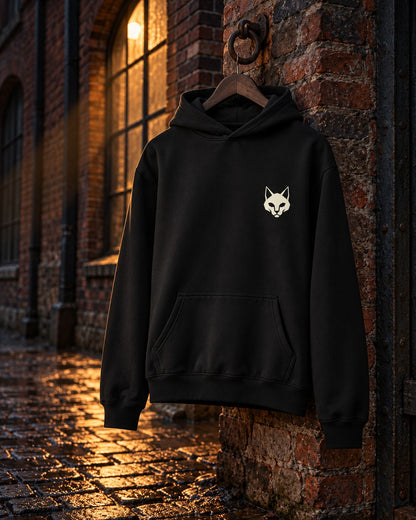 Cat Badge Hoodie, front print, black, hanging on a brick wall beside an arched window at night — AI-generated visual