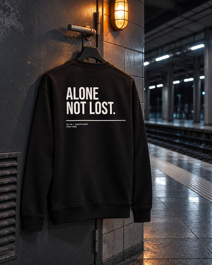 Alone Not Lost Sweatshirt, back print, black, hanging on a wall hook under a lamp on a train platform — AI-generated visual