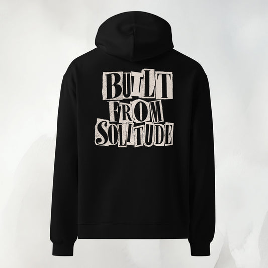 Back print of the Built From Solitude paste-up hoodie in black: hand-cut letters stacked into the words BUILT FROM SOLITUDE